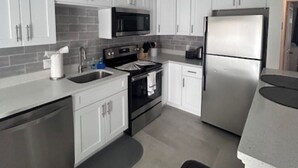 A modern kitchen with white cabinets, stainless steel appliances, and a grey countertop. - Updated 1BR Across from Ocean – Prime Deerfield Beach Location (Deerfield Beach)
