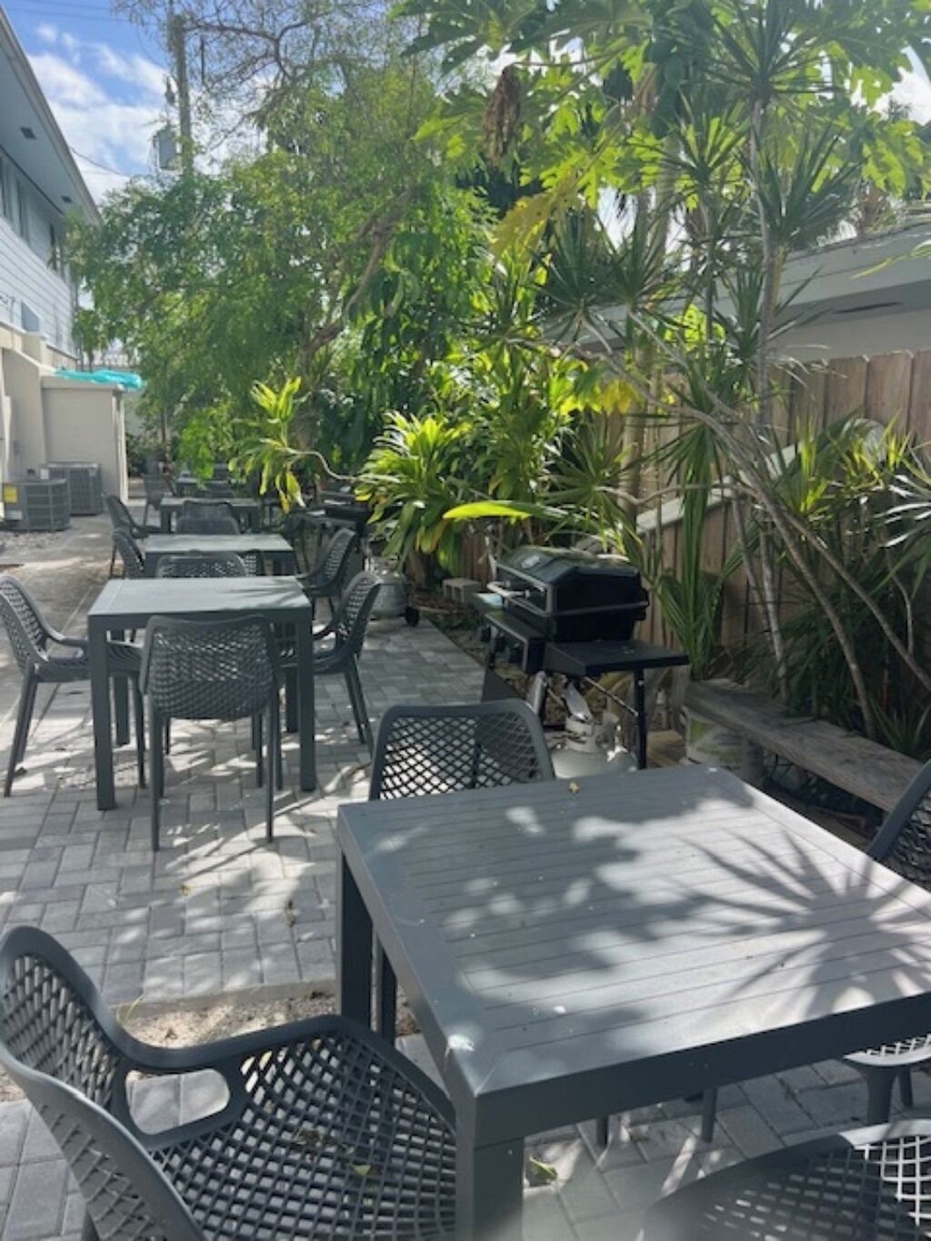 An outdoor patio area with tables and chairs, surrounded by lush greenery and a barbecue grill.
