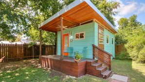 Ein kleines, eingeschossiges Haus mit Veranda, Holztreppe und einem umzäunten Garten.