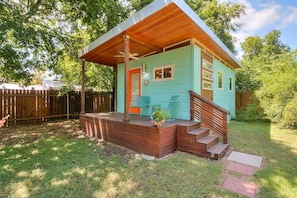 Ein kleines, eingeschossiges Haus mit Veranda, Holztreppe und einem umzäunten Garten.