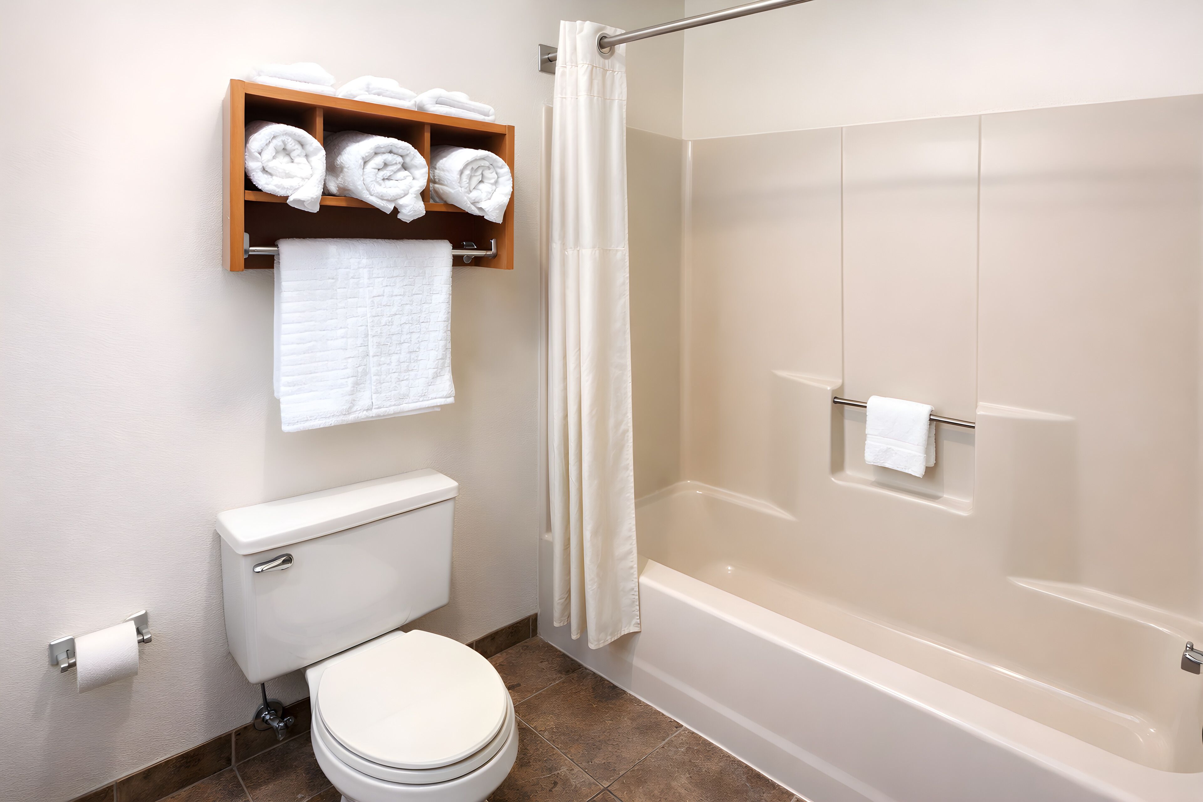 Un baño con inodoro, ducha, toallero con toallas y dispensador de papel higiénico.