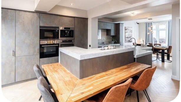 A modern kitchen with a central island, built-in appliances, and a dining area with a wooden table and chairs. - Large detached home for families and group stays (Hoyland)