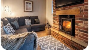 A living room with a fireplace, a sofa, a television, and a framed picture on the wall. - Large detached home for families and group stays (Hoyland)