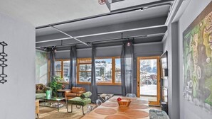 Ein modernes Interieur mit Esstisch, Stühlen, einer Couch und einem großen Fenster mit Blick auf eine verschneite Landschaft.