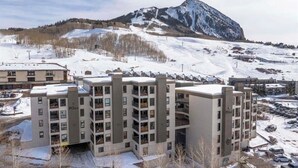 Ein mehrstöckiges Hotel mit modernem Design, gelegen in einer verschneiten Gegend mit einem Berg im Hintergrund.