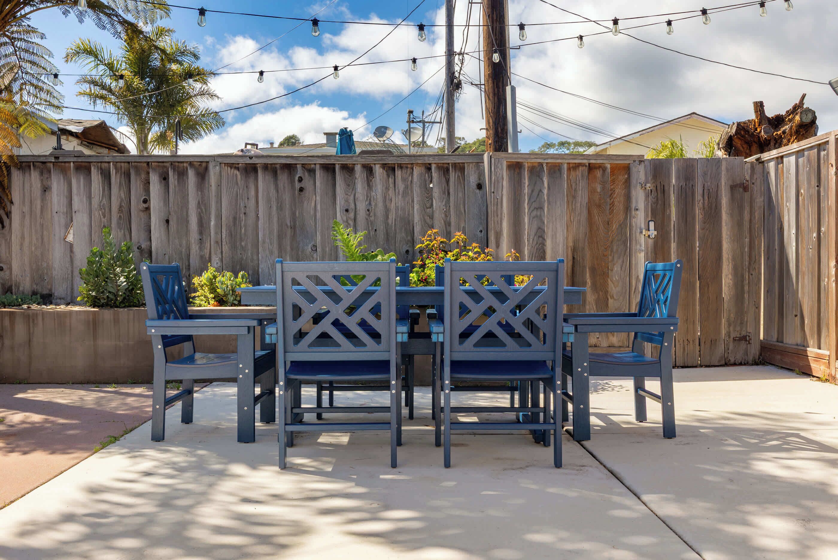 A patio with a wooden fence, outdoor furniture, and string lights.