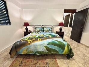 A bedroom with a bed, two nightstands, a lamp, a patterned rug, and a door. - Vieques BioBay B&B, The Coqui Room:Sleep Under the Stars, Paddle the Glowing Bay (Vieques)