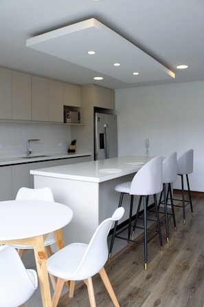 Une cuisine moderne avec un îlot central, des tabourets de bar blancs et une table à manger en bois.