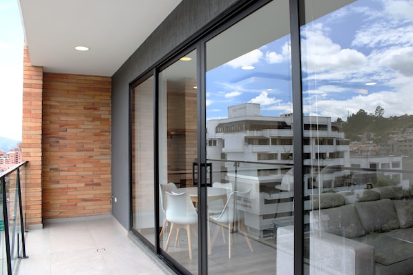 Un balcon avec une porte vitrée, un mur en briques et une vue sur des immeubles et des arbres.