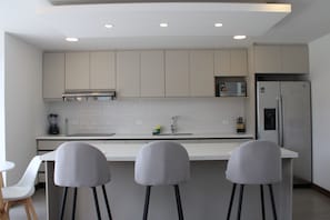 Une cuisine moderne avec des armoires blanches, un réfrigérateur en acier inoxydable et un plan de travail blanc.