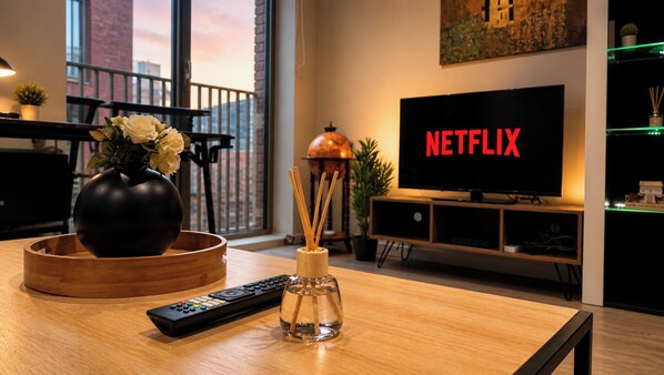 A modern living room with a wooden coffee table, a vase with flowers, a remote control, and a TV displaying the Netflix logo. - Canal-Side Apartment with Private Terrace - Castlefield - Business & Long Stays (Greater Manchester)