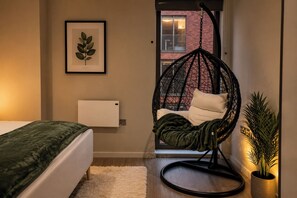 A bedroom with a bed, a hanging chair, a radiator, and a framed plant. - Canal-Side Apartment with Private Terrace - Castlefield - Business & Long Stays (Greater Manchester)