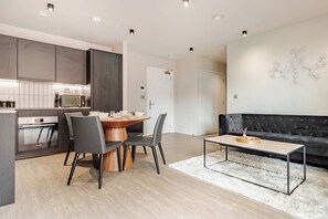 A modern kitchen with dark cabinets, a dining table with chairs, a sofa, and a coffee table. - Canal-Side Apartment with Private Terrace - Castlefield - Business & Long Stays (Greater Manchester)
