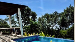 A swimming pool with a tiled deck, a covered seating area, and a table with a drink and lime slices. - Infinity Pool & Ocean View - Sunrise (Roatan)
