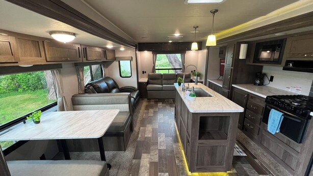 A compact RV kitchen with a dining area, a sink, and a stove. - EastToWest Glamping camper - Site #15 (Klamath)