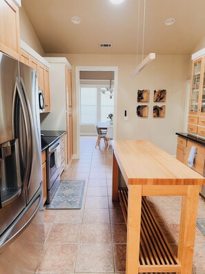 Eine moderne Küche mit einem Edelstahl-Kühlschrank, Holzschränken, einer zentralen Kochinsel und einem Essbereich mit Blick zum Esszimmer.
