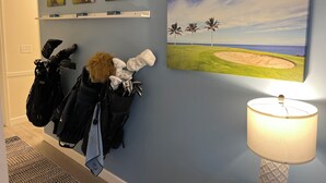 A room with a golf-themed wall art, a lamp, and a coat rack with bags. -  Scenic Golf Course View Retreat - UPDATED 2BR Condo-Close to Beach (North Myrtle Beach)