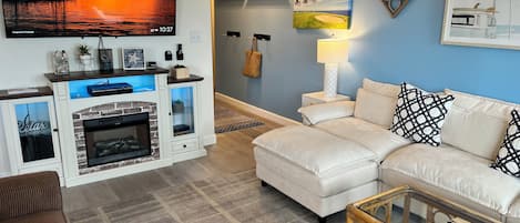 A living room with a fireplace, a sofa, a glass coffee table, and wall art.