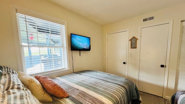 A bedroom with a bed, a TV on the wall, a window with blinds, and a door. -  Scenic Golf Course View Retreat - UPDATED 2BR Condo-Close to Beach (North Myrtle Beach)