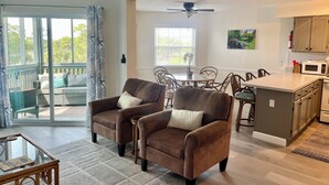 A spacious living area with a sofa set, a dining table, and a kitchen area with a microwave. -  Scenic Golf Course View Retreat - UPDATED 2BR Condo-Close to Beach (North Myrtle Beach)