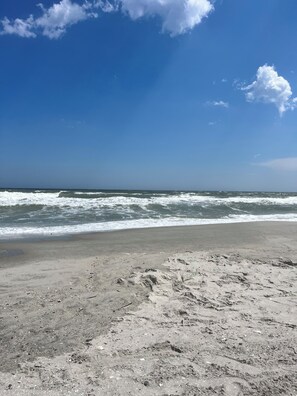 Ein Strand mit Wellen, blauem Himmel und sandigem Ufer.