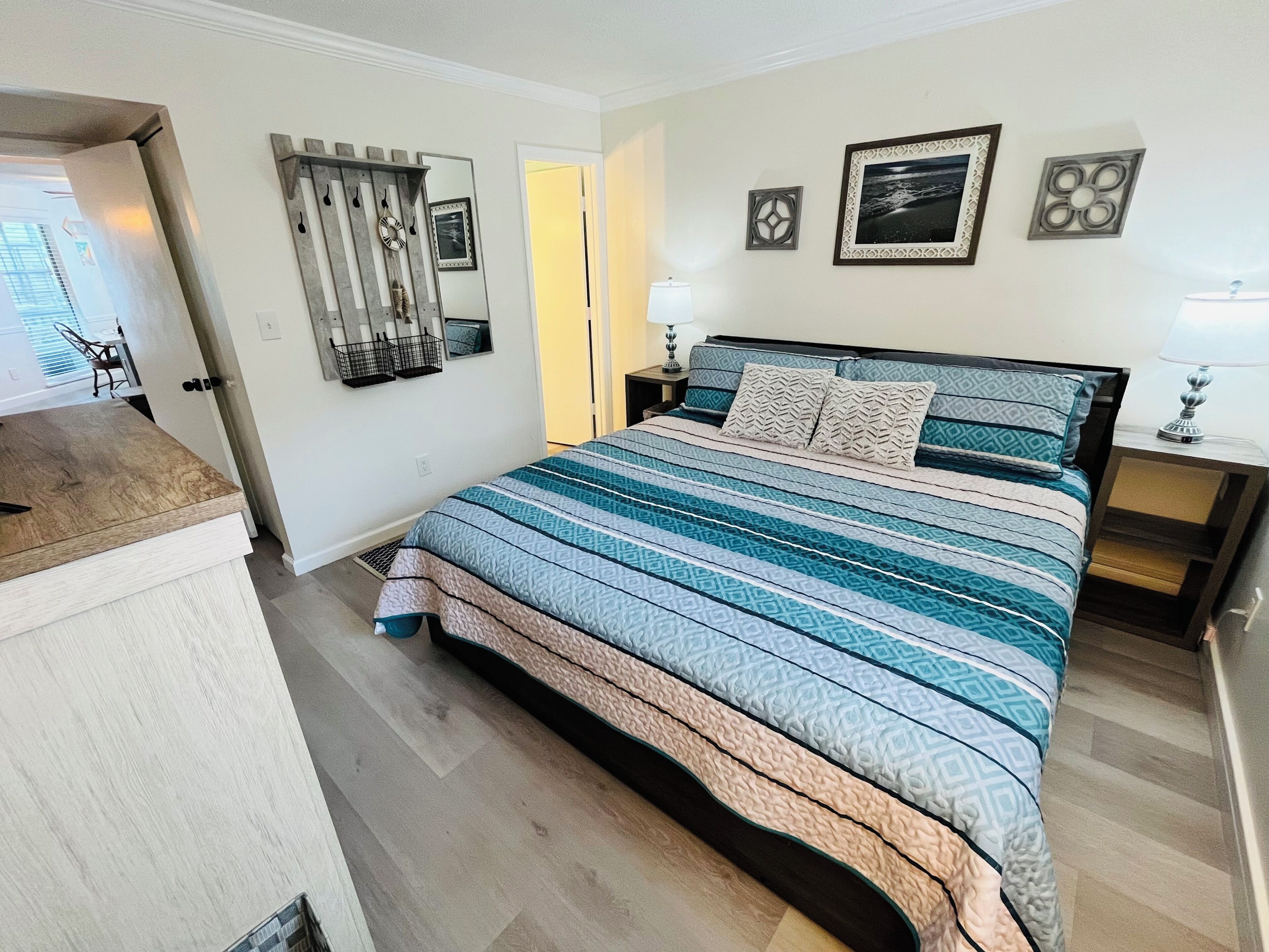 A bedroom with a large bed, a bedside table, a nightstand, a mirror, and a door leading to another room.