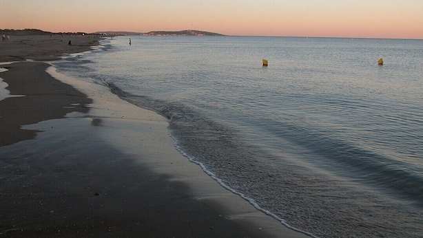 A beach with calm waters, a sandy shore, and a distant shoreline.