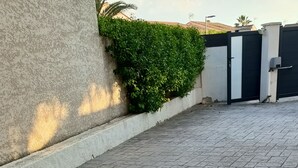 A paved walkway with a hedge and a gated entrance.