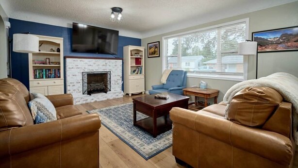 A living room with leather sofas, a fireplace, a flat-screen TV, and a large window with blinds.