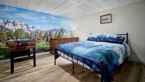 A bedroom with a bed, a wooden dresser, a foosball table, and a large window with a mountain view.
