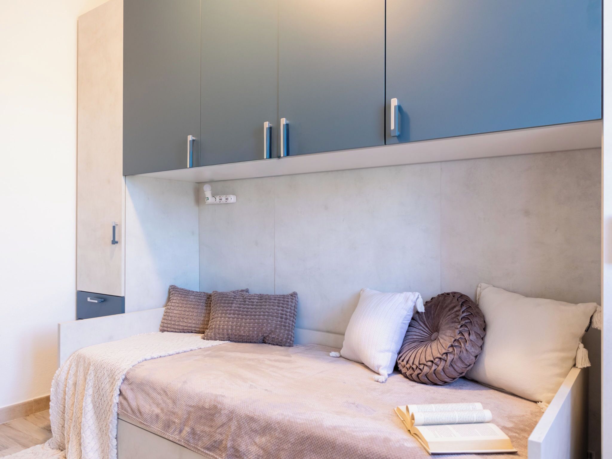 Um quarto com cama, almofadas, mesa de cabeceira e guarda-roupa.