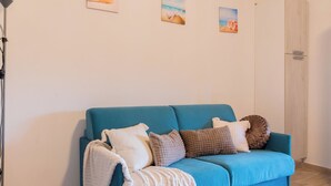 Een kamer met een blauwe bank, een lamp en drie aan de muur bevestigde foto’s van landschappen.