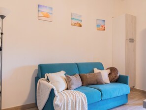 A room with a blue sofa, a lamp, and three wall-mounted pictures depicting landscapes. - Perla San Teo by Interhome (San Teodoro)