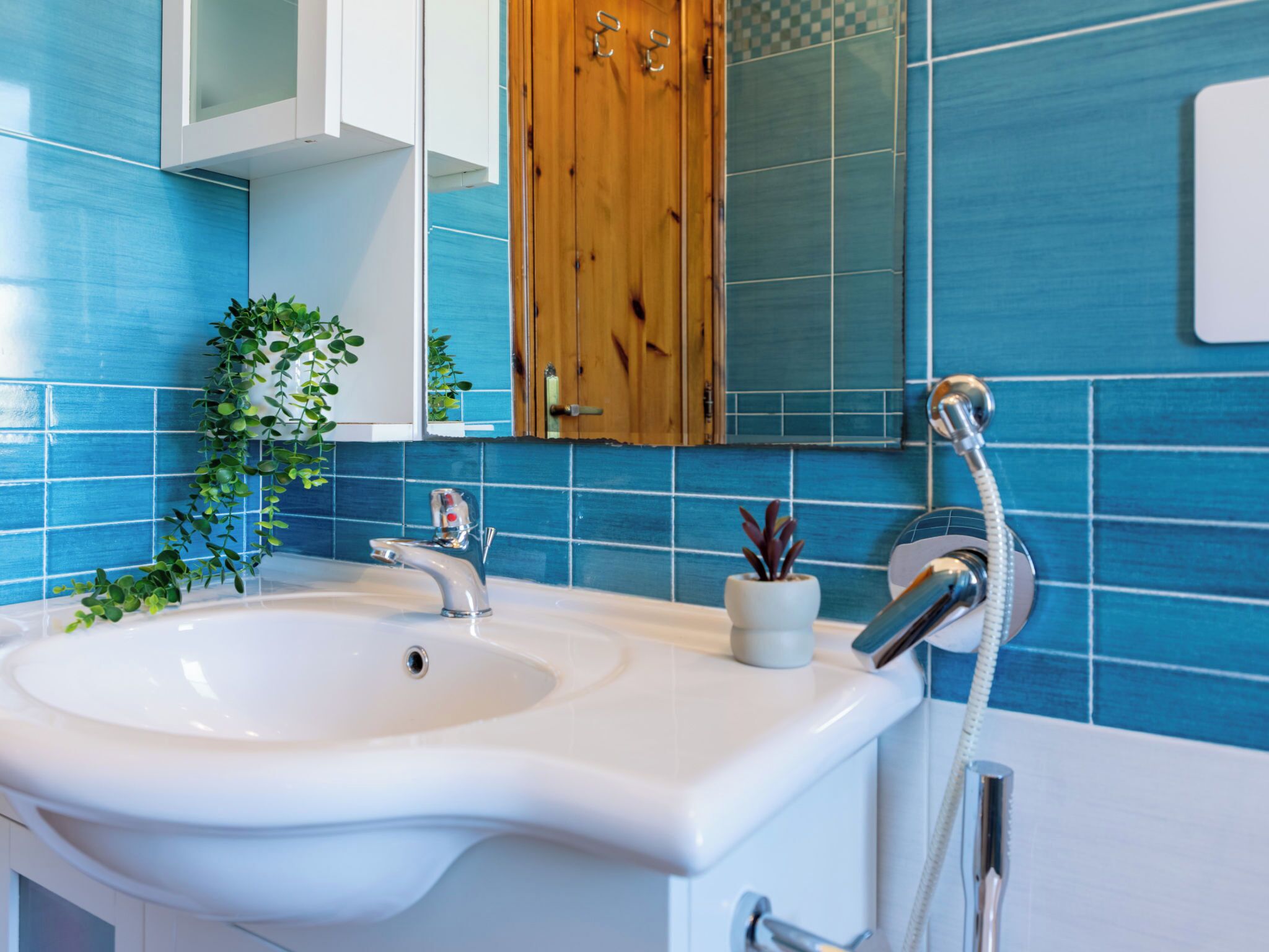 Une salle de bain avec un lavabo blanc, un meuble en bois et un mur recouvert de carreaux bleus.