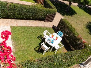 Een terras met een tafel en stoelen, omringd door keurig onderhouden hagen en een stenen pad.