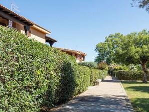 A pathway leading to a building with a tiled roof and stone walls, surrounded by well-maintained hedges and trees. - Perla San Teo by Interhome (San Teodoro)