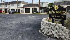A sign for Lago Bonito Townhomes with a parking lot and residential buildings in the background.