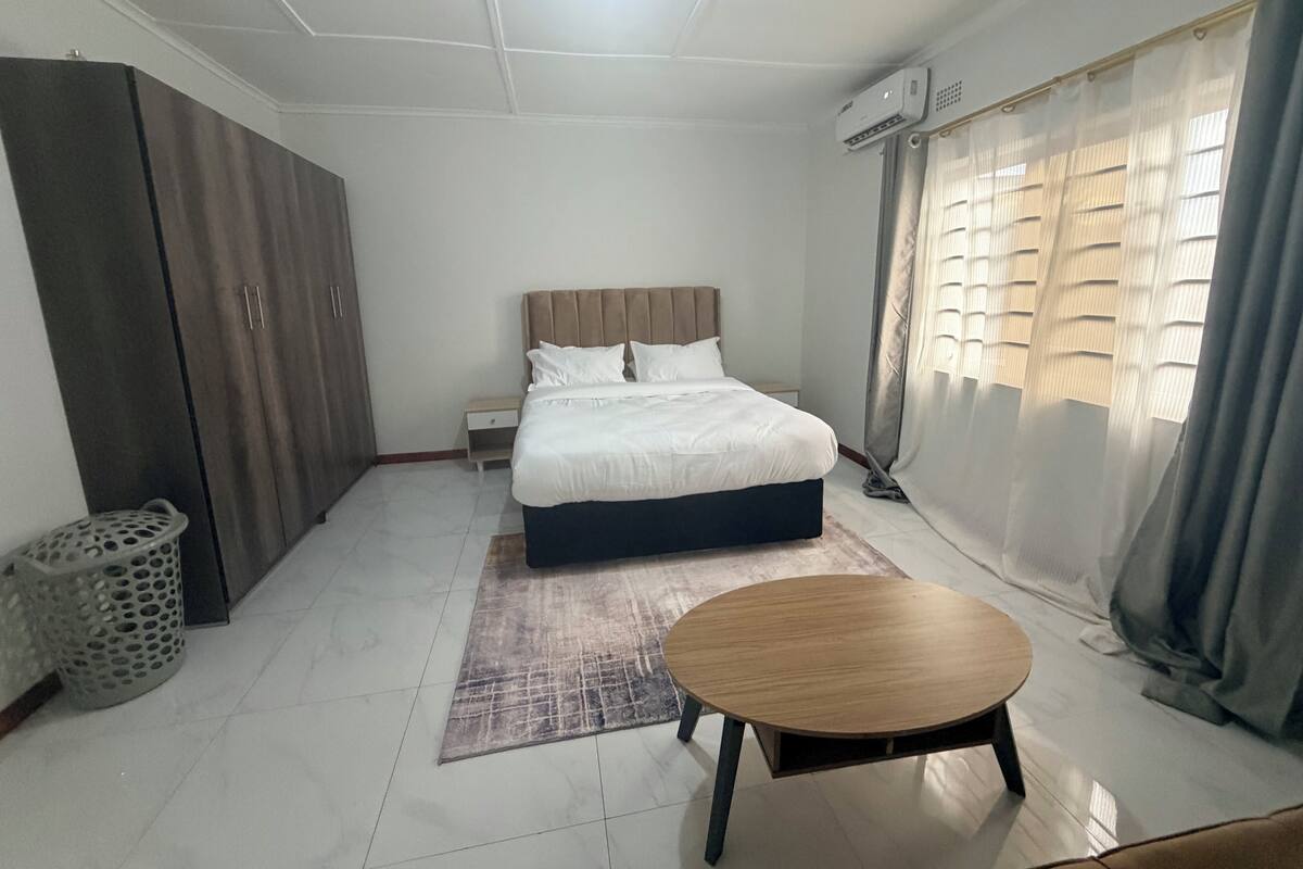 A bedroom with a bed, a small table, a wardrobe, and a window with curtains.