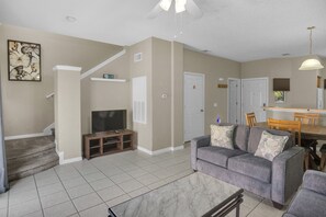 A living room with a gray sofa, a TV, and a staircase. - Minutes to Disney! Gated 3BR Resort Townhome (Kissimmee)
