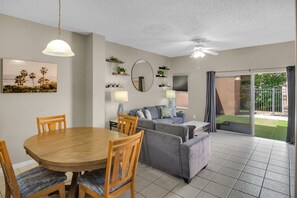 A modern living room with a dining table, chairs, a sofa, a ceiling fan, and a sliding glass door leading to a balcony. - Minutes to Disney! Gated 3BR Resort Townhome (Kissimmee)