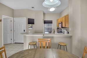 A kitchen with wooden cabinets, a white countertop, and a dining area with a wooden table and chairs. - Minutes to Disney! Gated 3BR Resort Townhome (Kissimmee)