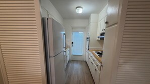 A narrow kitchen with a refrigerator, stove, and cabinets.