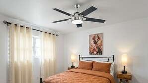 A bedroom with a bed, two bedside tables, a ceiling fan, and a window with curtains.