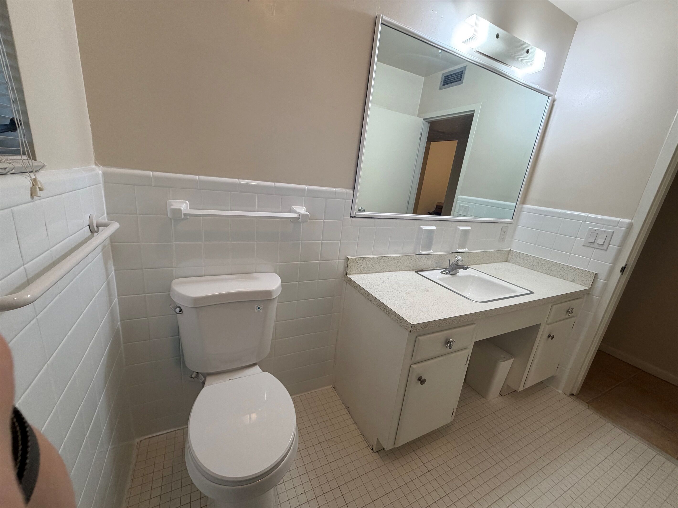 A bathroom with a toilet, sink, mirror, and tiled walls.