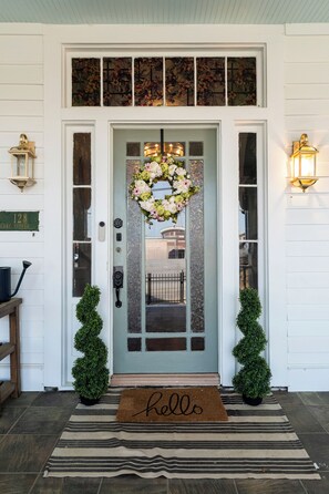 A front door with a doormat, a wreath, and two potted plants.