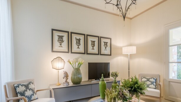 A living room with a sofa, a coffee table, a TV, framed artwork, and a chandelier. - Charming Lucca Villa With Garden (Lucca)