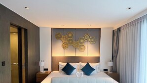Quarto de hotel moderno com uma cama grande, duas mesas de cabeceira, um objeto decorativo na parede e vista para o exterior.