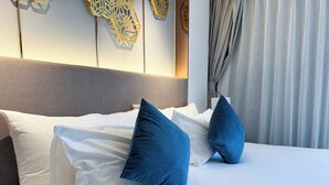 Quarto de hotel com cama, almofadas, cabeceira, painéis decorativos na parede e cortinas.