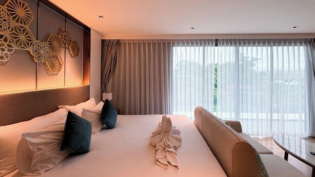 Quarto de hotel com uma cama grande, um sofá, uma mesa pequena e um painel decorativo na parede.