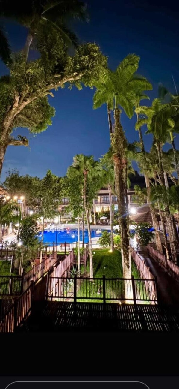 Ein Nachtblick auf ein Resort mit Palmen, einem Pool und einer Holzterrasse.
